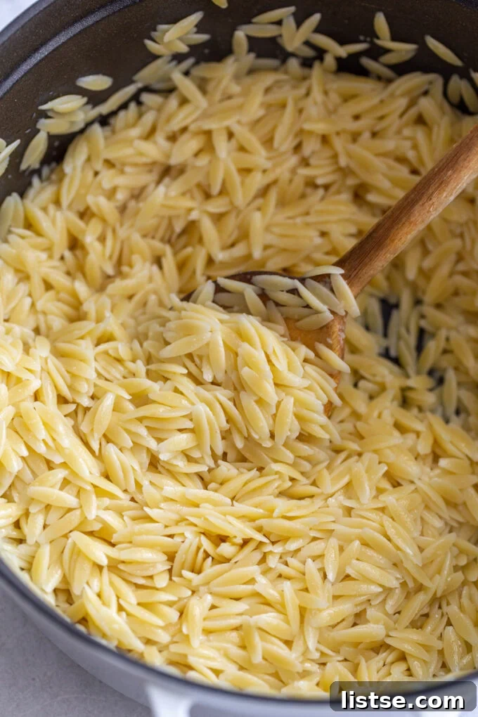 Stirring cooked orzo with a wooden spoon in a pot