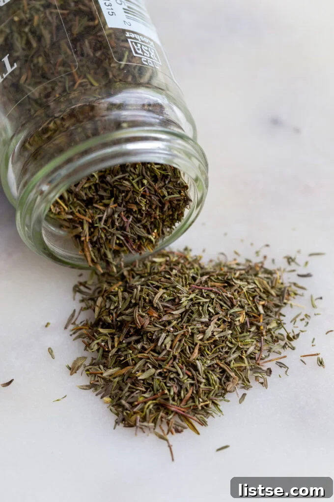 Top Thyme Alternatives 3 Dried thyme spilling out of a clear glass spice jar onto a wooden surface.