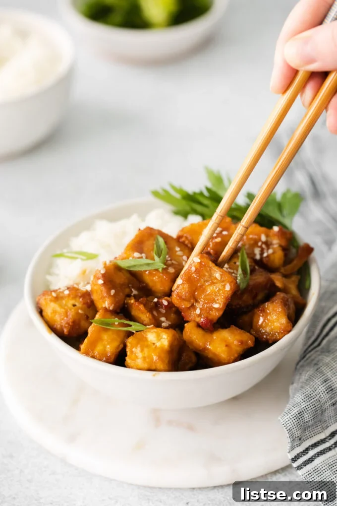 Close-up of a person using chopsticks to pick up a cube of glossy, spicy air fryer tofu
