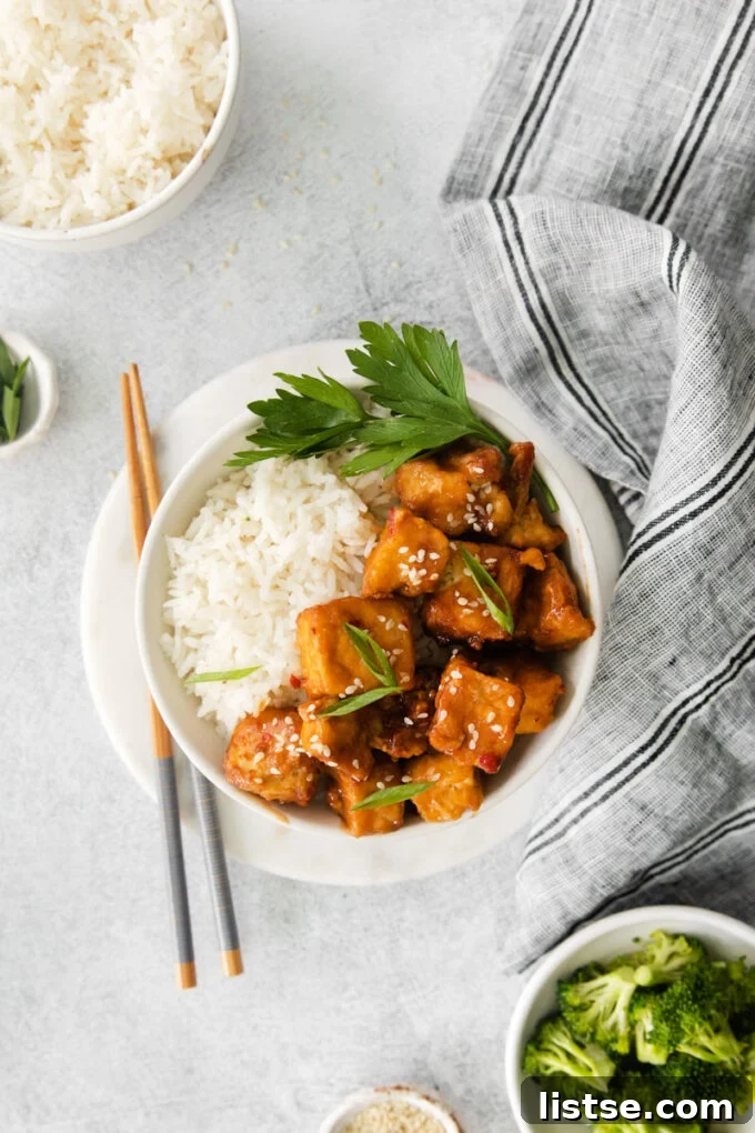 Air fryer spicy tofu with white rice, garnished with green onions and sesame seeds, served with chopsticks