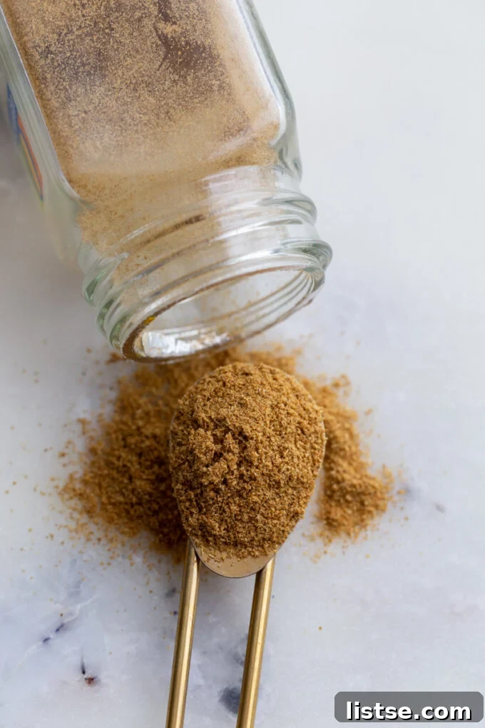 A scoop of ground cumin next to an open jar of cumin and scattered cumin seeds, illustrating its use in cooking.