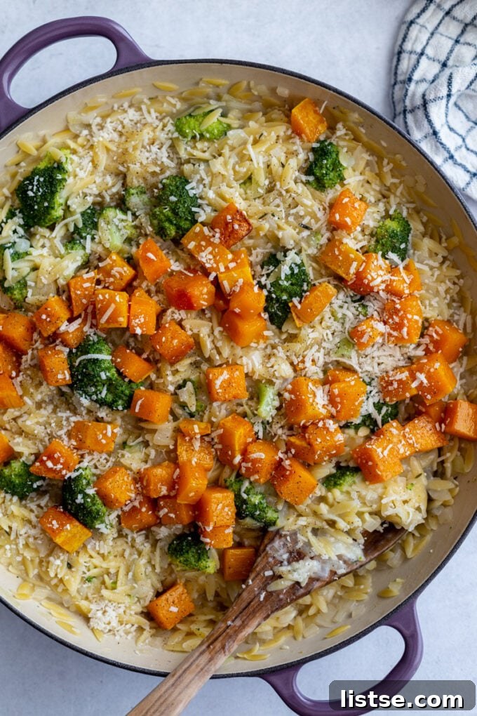 Golden Cheesy Butternut Orzo 3 A large purple skillet brimming with creamy parmesan orzo, generously mixed with vibrant butternut squash and crisp broccoli florets, ready to be served.