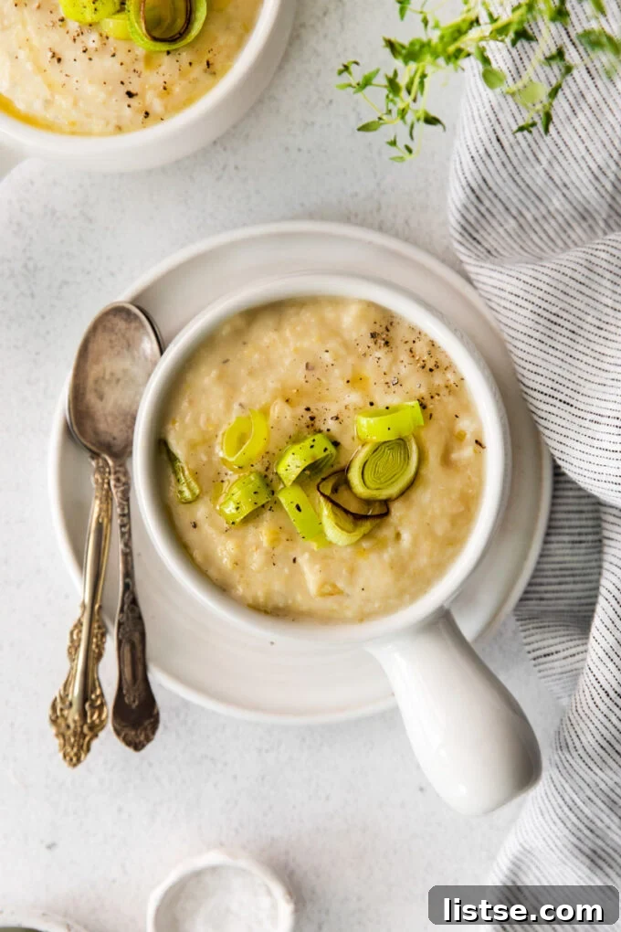 A serving of creamy Vegan Potato Leek Soup in a small white bowl, garnished with fresh herbs.