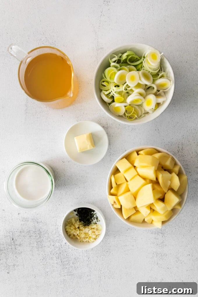 Various fresh ingredients laid out on a cutting board, including leeks, potatoes, garlic, and herbs, ready for making vegan potato leek soup.