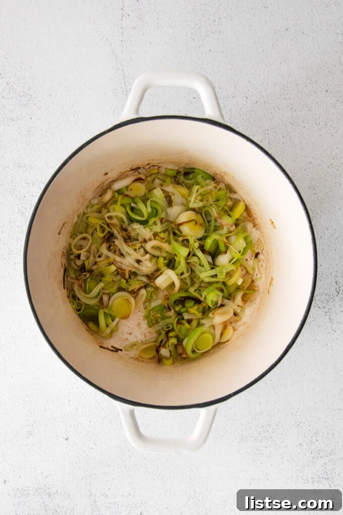 Leeks being sautéed in a large pot with melted butter, releasing their sweet aroma.