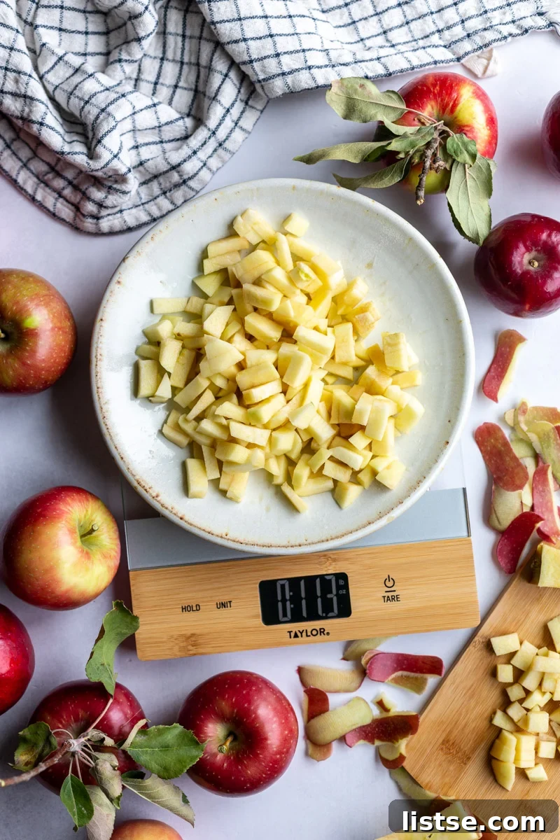 apple pieces on a plate on a kitchen scale with lots of apples and apple scrapes around the scene. towel in the corner and fresh apples around