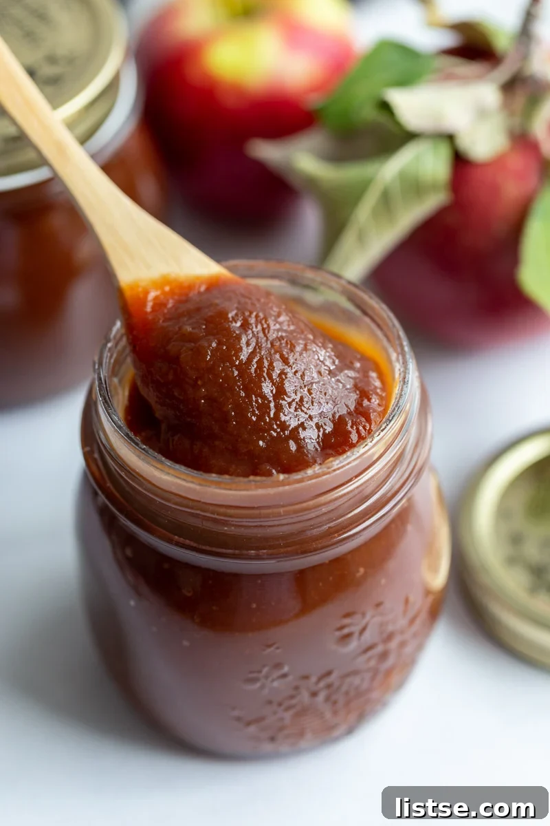 apple butter in a small glass jar with a small spoon scooping some out. apples in the background
