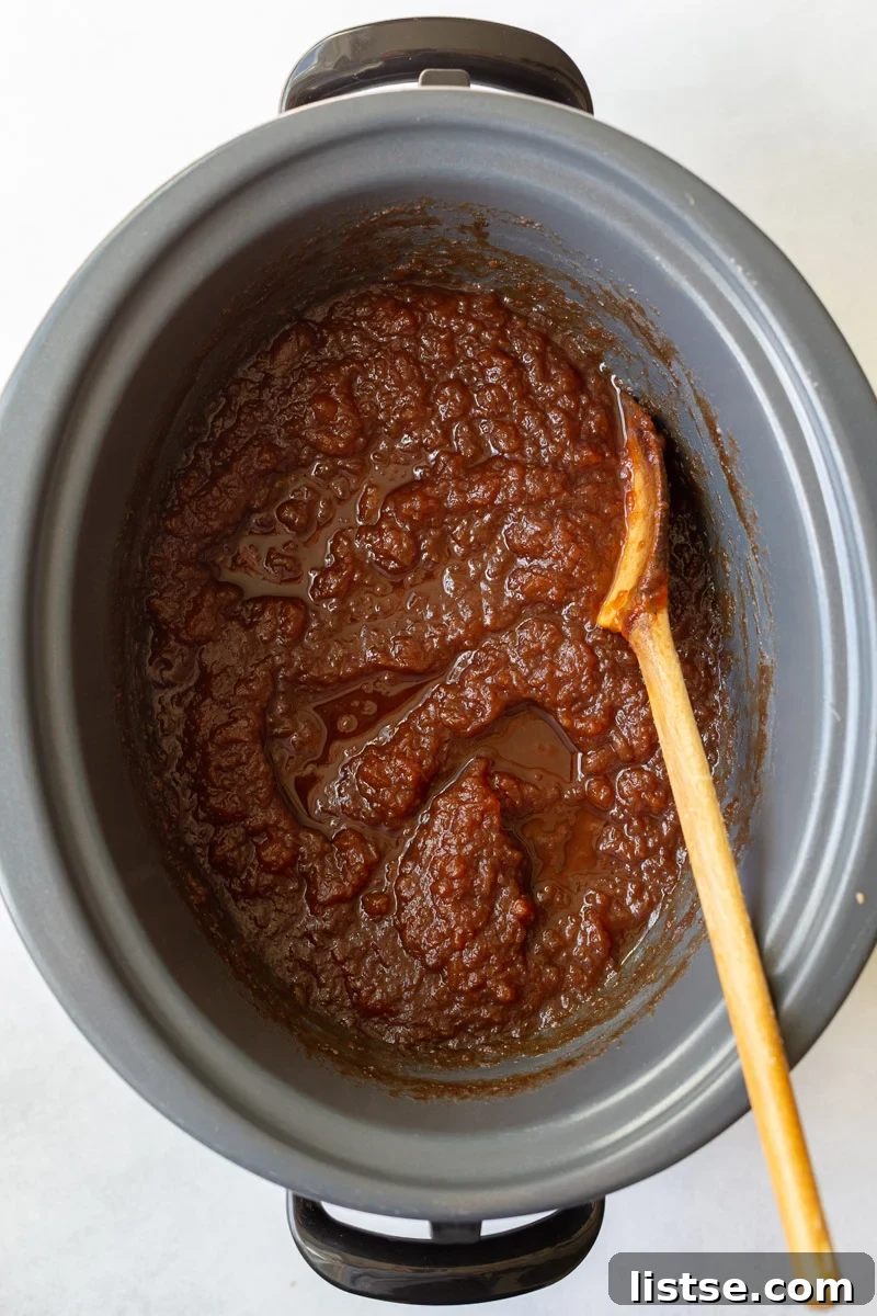 unblended apple butter in a crockpot with a wooden spoon on the side