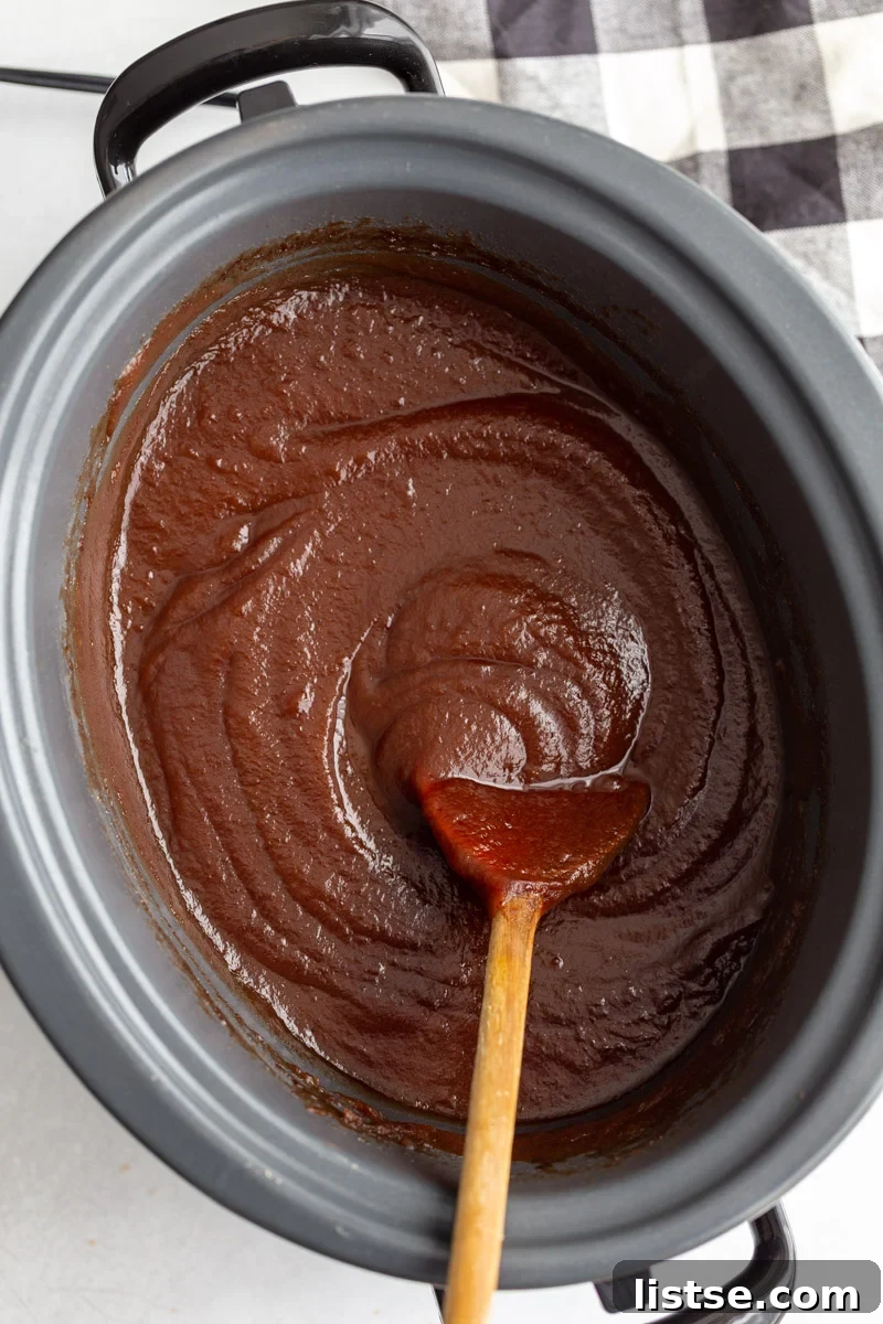 blended and smooth apple butter in a crockpot with a wooden spoon on the side