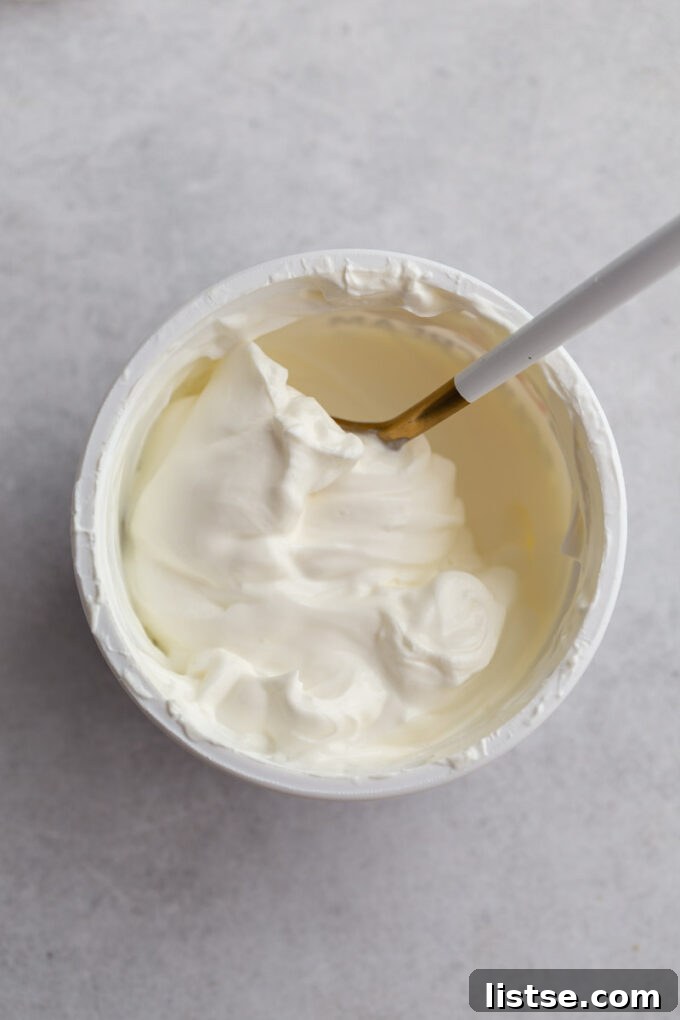 A top-down shot of a tub of sour cream with a spoon swirled in it, illustrating its creamy texture before freezing.