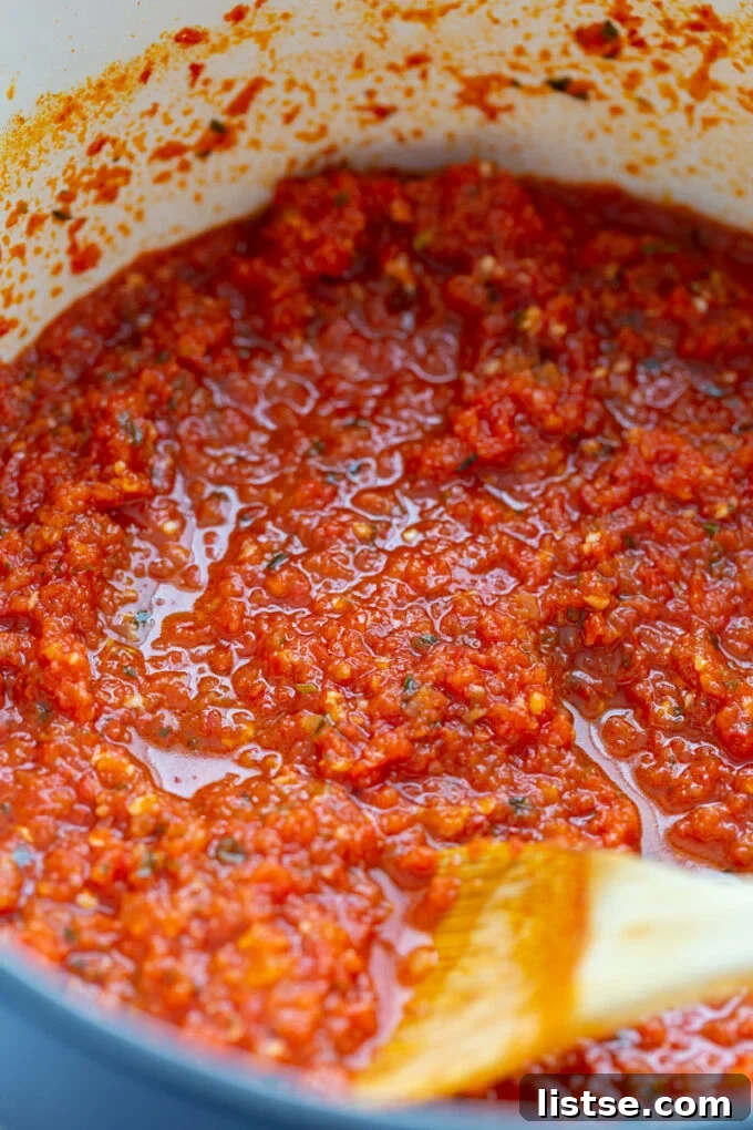 A large pot on the stove, filled with vibrant red Pomodoro sauce being stirred with a wooden spoon.