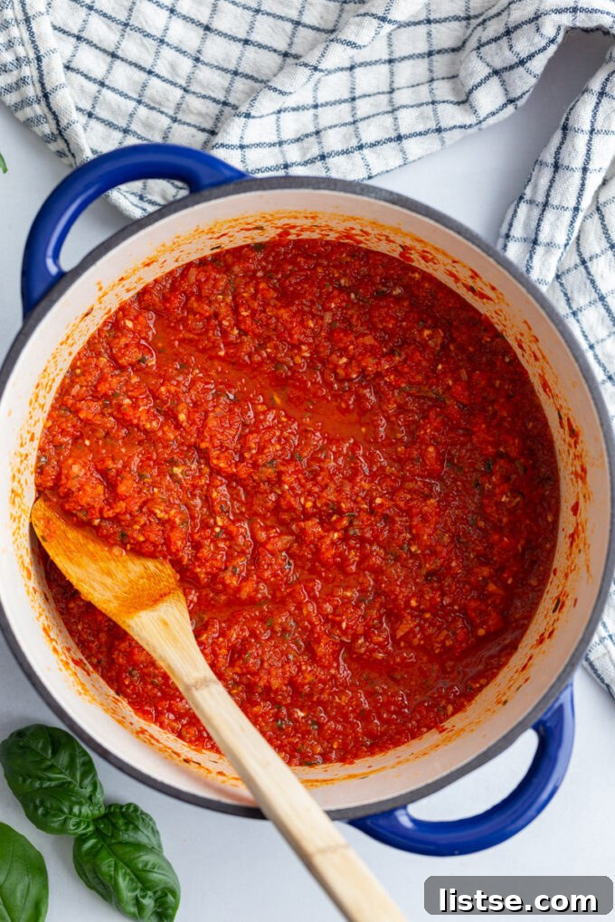 A wooden spoon stirring thick red Pomodoro sauce in a large pot on the stove.