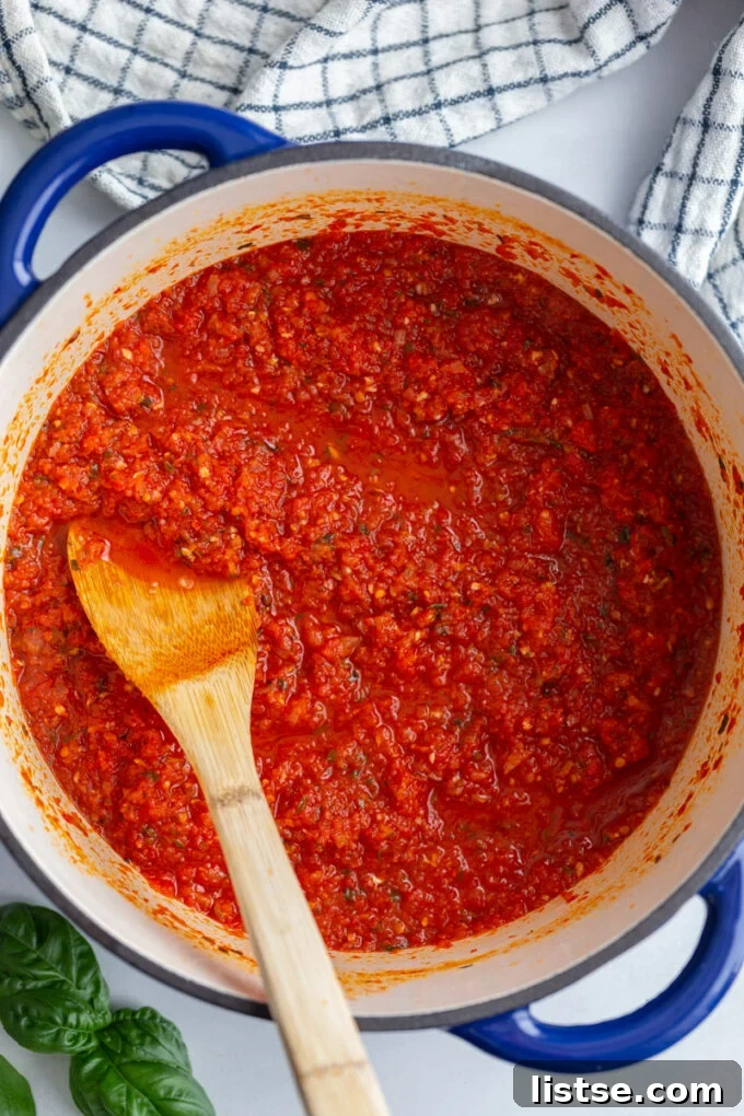 Pomodoro sauce simmering in a large pot with a wooden spoon resting in it.
