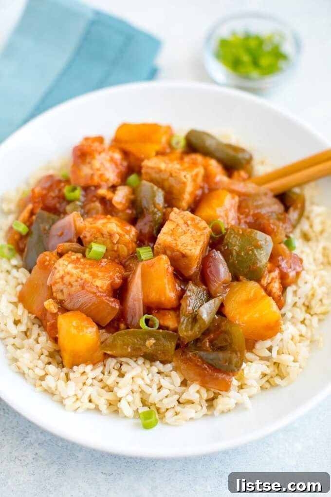Effortless Vegetarian Crockpot Feasts 19 Sweet and sour tempeh served over fluffy white rice, garnished with fresh herbs.