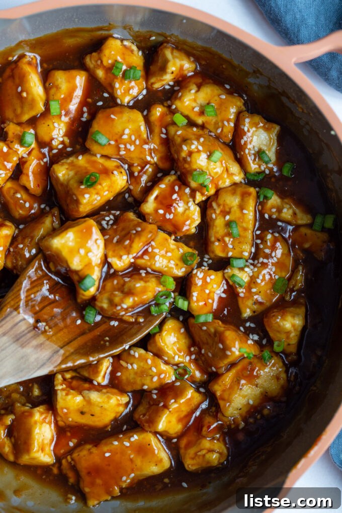 Golden Crispy General Tso Tofu 5 stirring tofu with a wooden spoon in a skillet