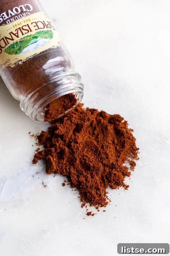 A small glass jar filled with ground cloves, showcasing their fine texture and rich brown color.