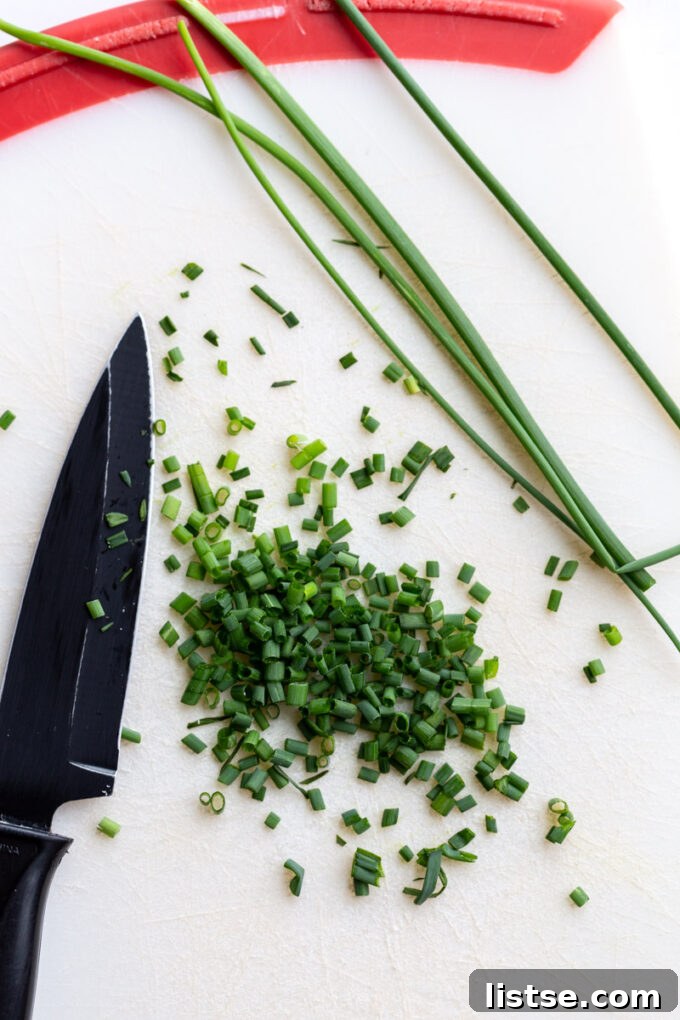 Beyond Chives: Flavorful Substitutions 2 Freshly diced chives next to a bunch of whole chives on a cutting board with a small knife, ready for cooking or garnish.