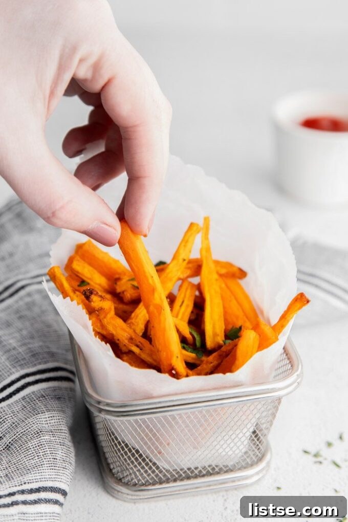 A woman's hand reaching into an air fryer basket to grab a perfectly cooked carrot fry.