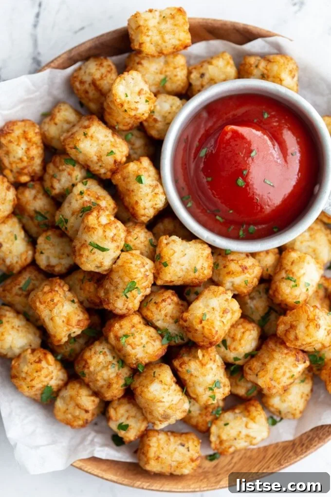 Crispy tater tots served hot with a dollop of ketchup on a white plate.