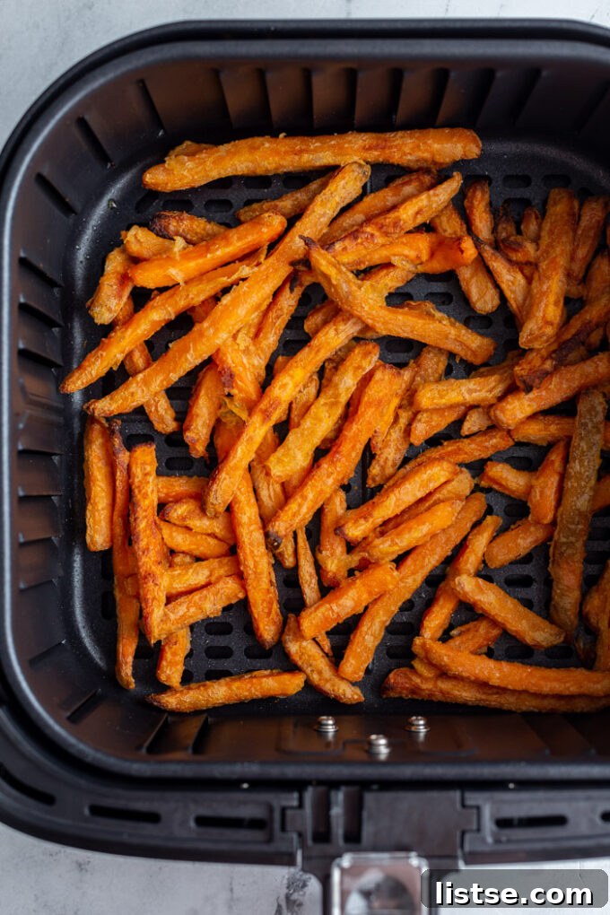 Basket of an air fryer filled with perfectly cooked sweet potato fries, crispy and golden.