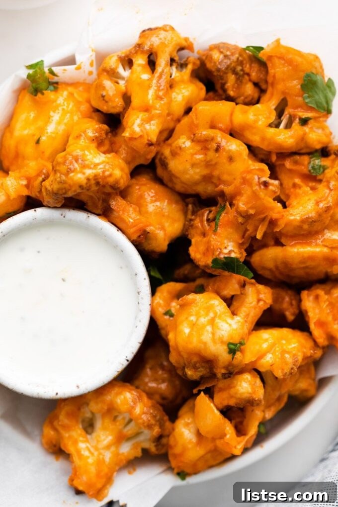 Crispy buffalo cauliflower florets served with a creamy dipping sauce on a plate.