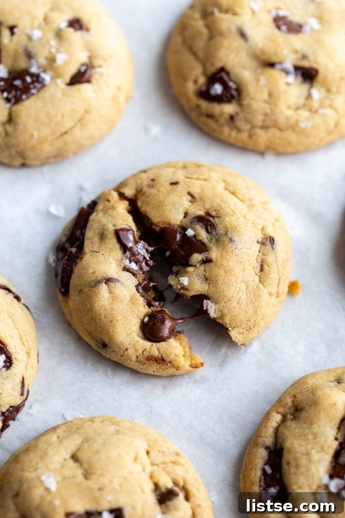 Close-up of freshly baked vegan chocolate chunk cookies on a white background, with one cookie perfectly cracked to reveal gooey melted chocolate inside.