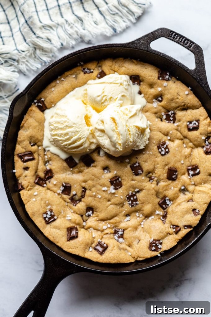 A warm, gooey vegan skillet cookie studded with chocolate chips, served hot in a cast iron pan, ready to be scooped.