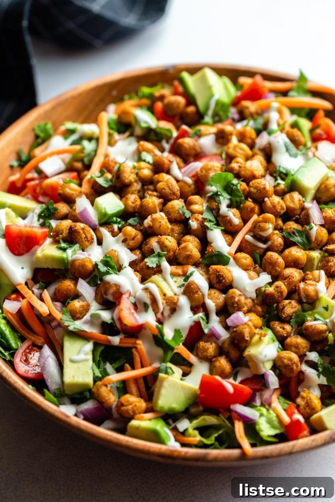 Inspired Chickpea Meals 16 A substantial salad presented in a rustic wood bowl, featuring crisp lettuce, various chopped vegetables, and a generous topping of roasted chickpeas, all beautifully drizzled with creamy vegan ranch dressing.