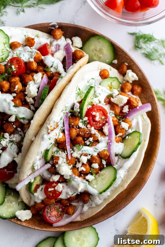 Inspired Chickpea Meals 17 A tantalizing gyro, generously filled with crispy chickpeas, fresh red onion, and creamy feta cheese, artfully arranged on a wooden plate.