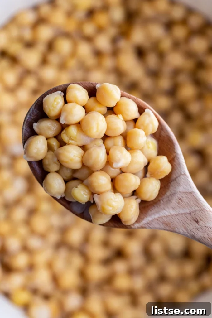 Inspired Chickpea Meals 6 A wooden spoon generously filled with tender cooked chickpeas, poised over a large pot of more chickpeas, highlighting abundance and readiness for use.