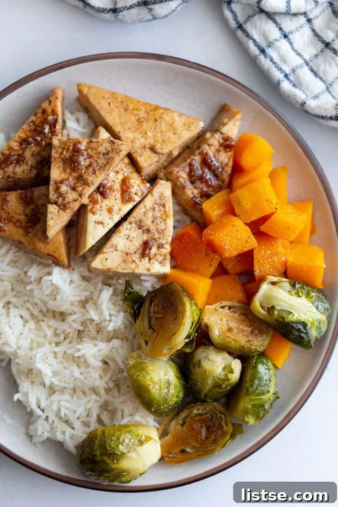 Tofu and veggies, including Brussels sprouts, served over rice in a bowl.