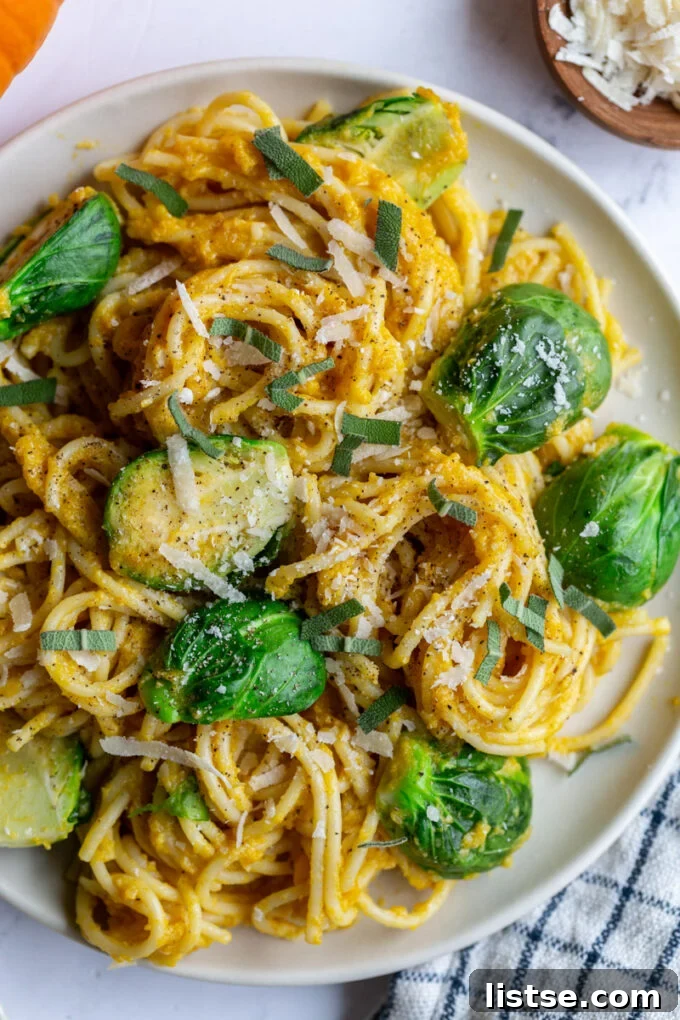 Large plate of spaghetti covered in pumpkin sauce with halved Brussels sprouts on top.