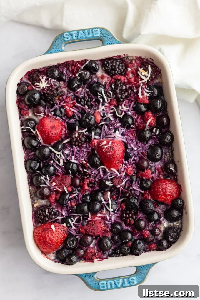 Mixed berry-topped baked oatmeal in a vibrant green casserole dish, ready to be served for a healthy breakfast.