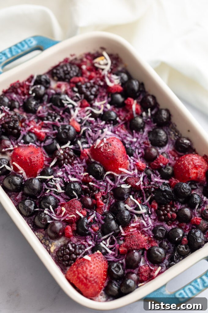Overhead shot of mixed berry baked oatmeal in a green staub casserole dish, garnished with fresh berries and ready for serving.