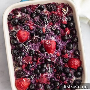 Mixed berry-topped baked oatmeal in a vibrant green casserole dish, ready to be served for a healthy breakfast.