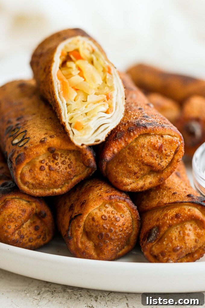 Stack of vegan egg rolls filled with colorful vegetables on a white serving plate, garnished with fresh herbs.