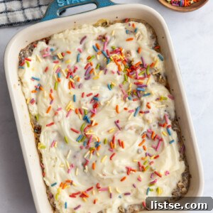 Casserole dish of baked oats topped with cream frosting and sprinkles with a bowl of sprinkles on the side