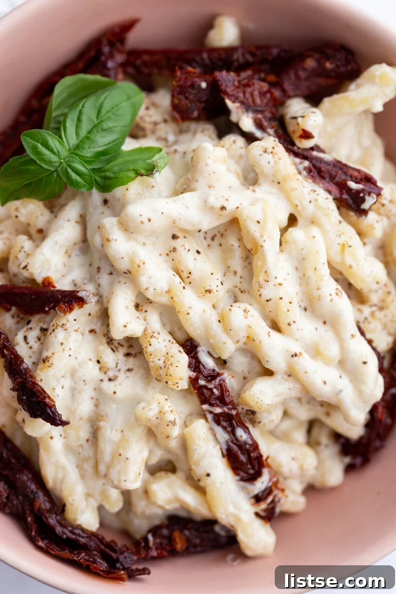 Velvety Vegan Alfredo 2 Delicious spiral pasta generously coated in a rich, creamy white sauce and garnished with vibrant sun-dried tomatoes.