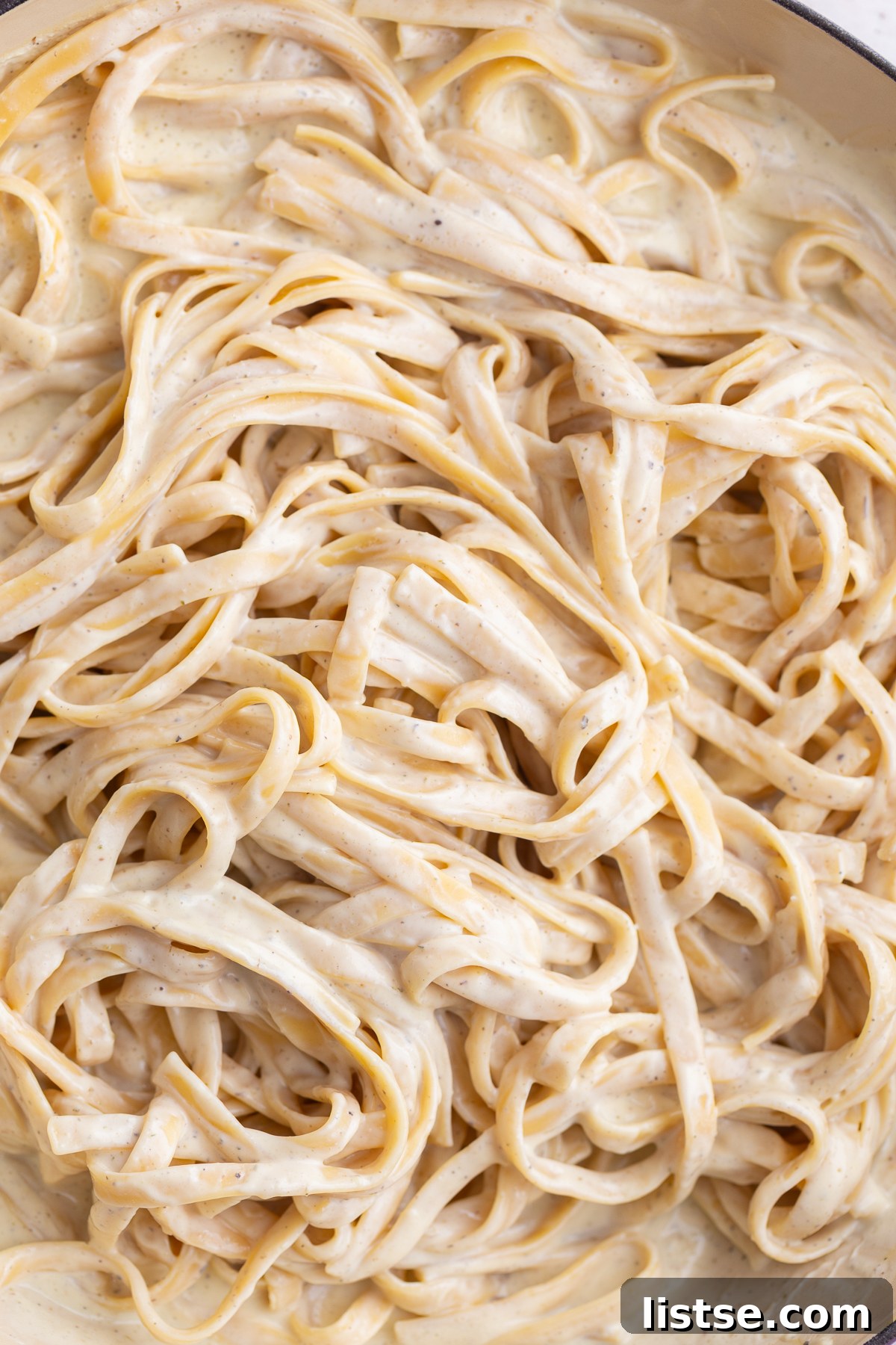 Velvety Vegan Alfredo 3 Freshly cooked pasta being tossed in a large pot with a rich, white creamy sauce, ready to be served.