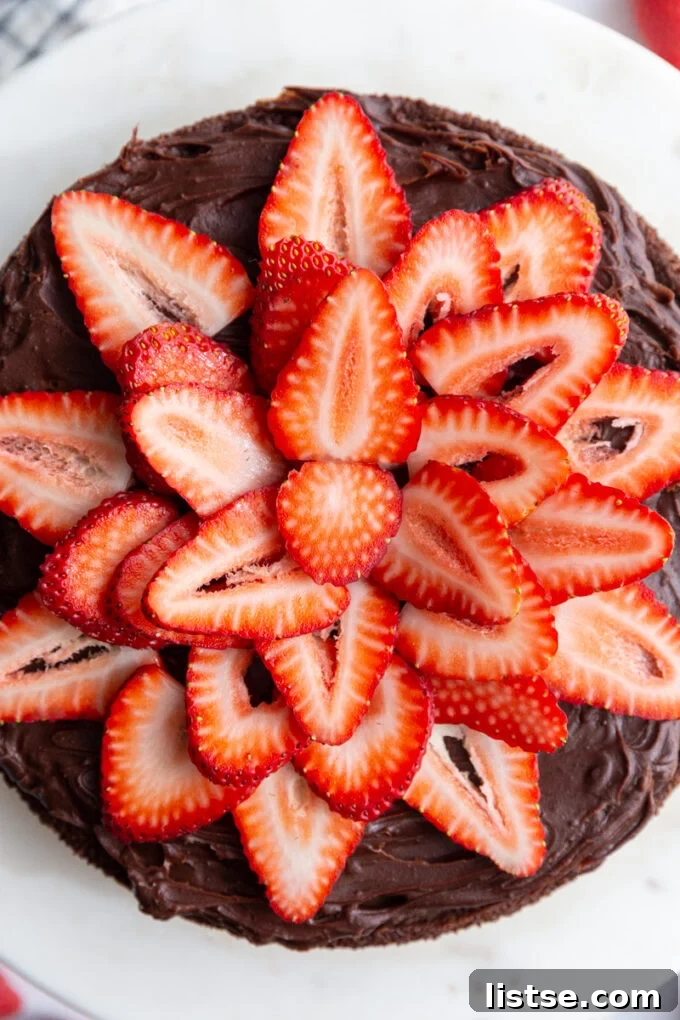 Decadent Vegan Gluten-Free Cake 4 Close-up of a frosted chocolate cake topped with sliced strawberries.