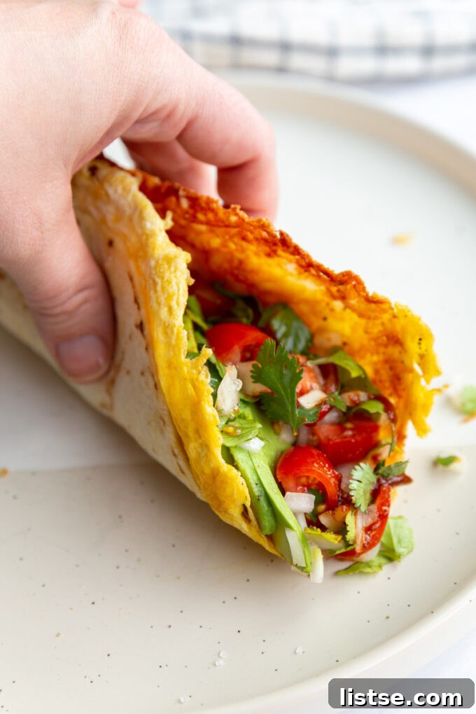 A hand holding a perfectly assembled breakfast taco, showcasing its vibrant fillings of egg, cheese, and various colorful vegetables.