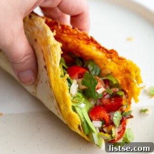 hand holding up a breakfast taco with lots of veggies in it