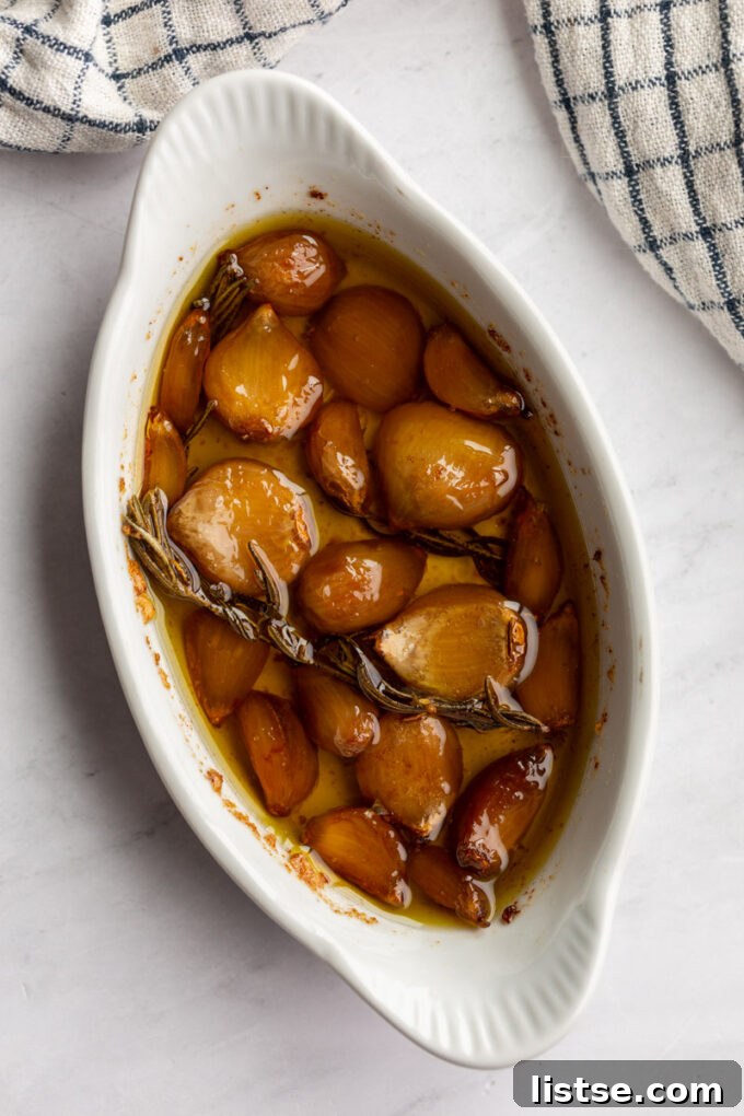 Golden, cooked garlic cloves submerged in olive oil in a white baking dish.
