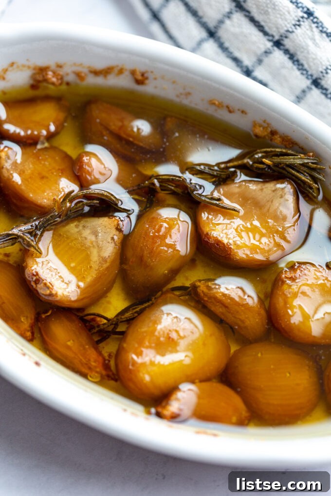 A white ceramic dish filled with golden garlic confit and sprigs of fresh rosemary.