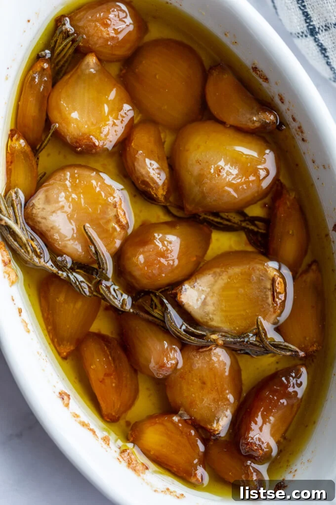 Garlic confit and rosemary sprigs in a white baking dish, ready for storage.