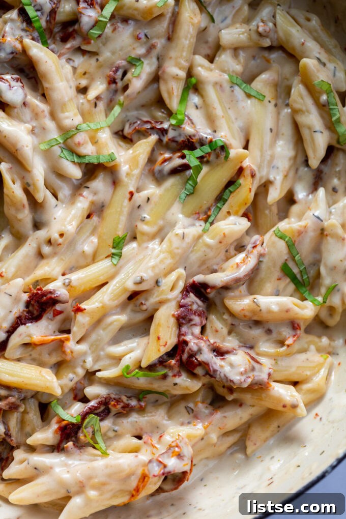 Close-up of penne pasta tossed in a creamy white sauce, ready to be served.