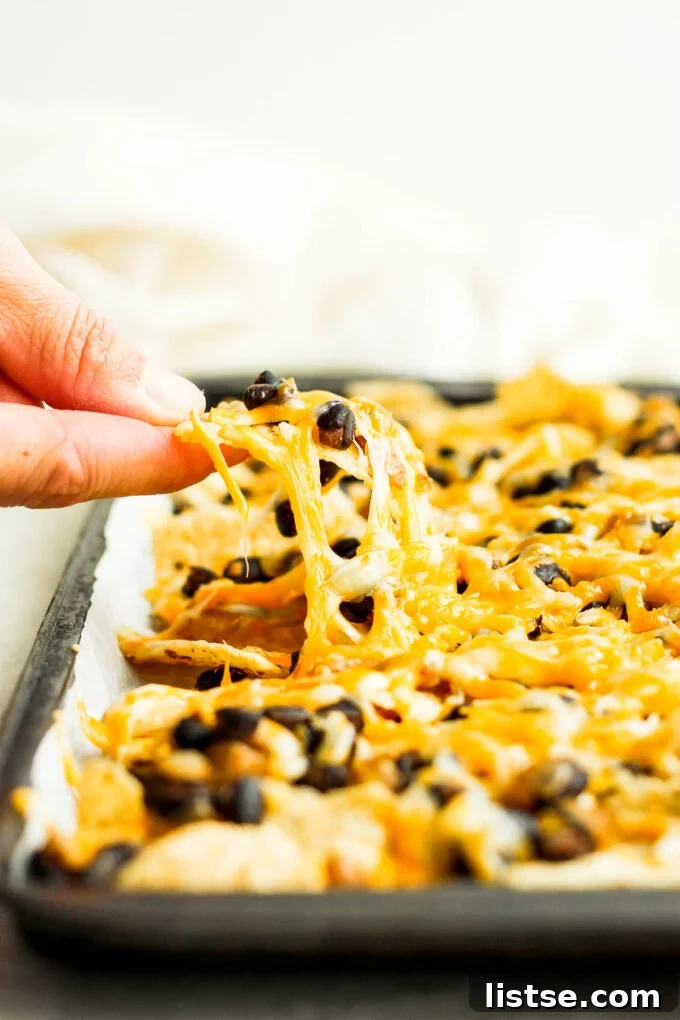 A woman's hand reaching for a perfectly loaded vegetarian nacho from a baking tray, showcasing its rich toppings and melted cheese.