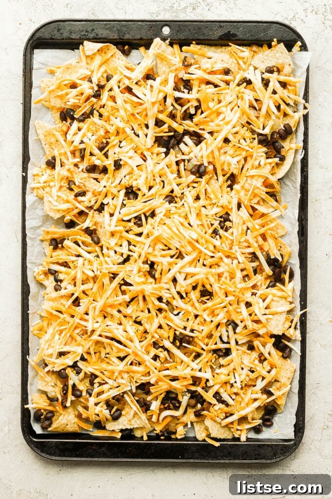 Assembling layers of tortilla chips and shredded cheese on a baking tray, a crucial step before adding bean mixture and baking.