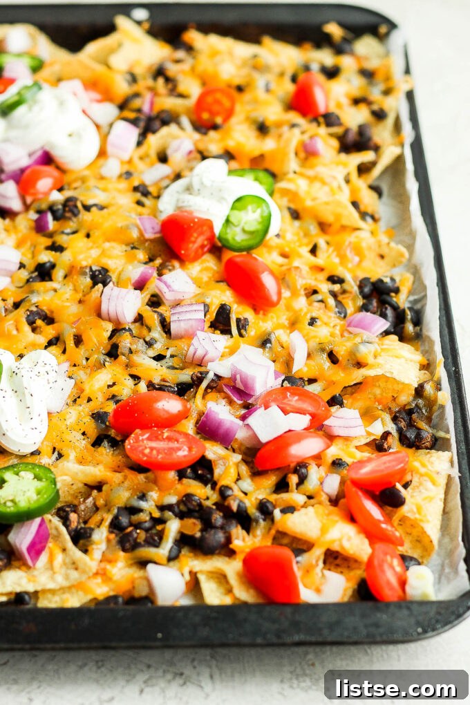 A close-up shot of vegetarian nachos loaded with melted cheese, black beans, and diced tomatoes, perfectly baked and ready to serve.