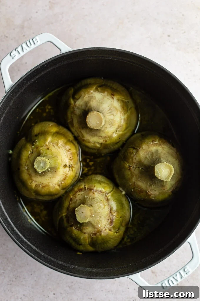 Roman Artichokes braising in a rustic cast iron pan, showing the cooking process